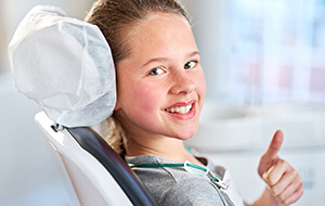 Girl in dental chair giving thumbs up